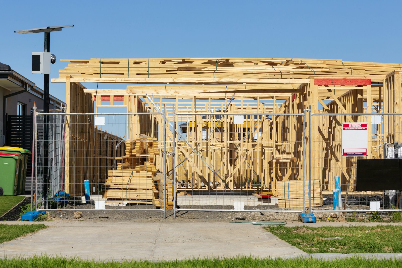 Wood-framed accessory structure under construction behind a temporary fence with a posted permit