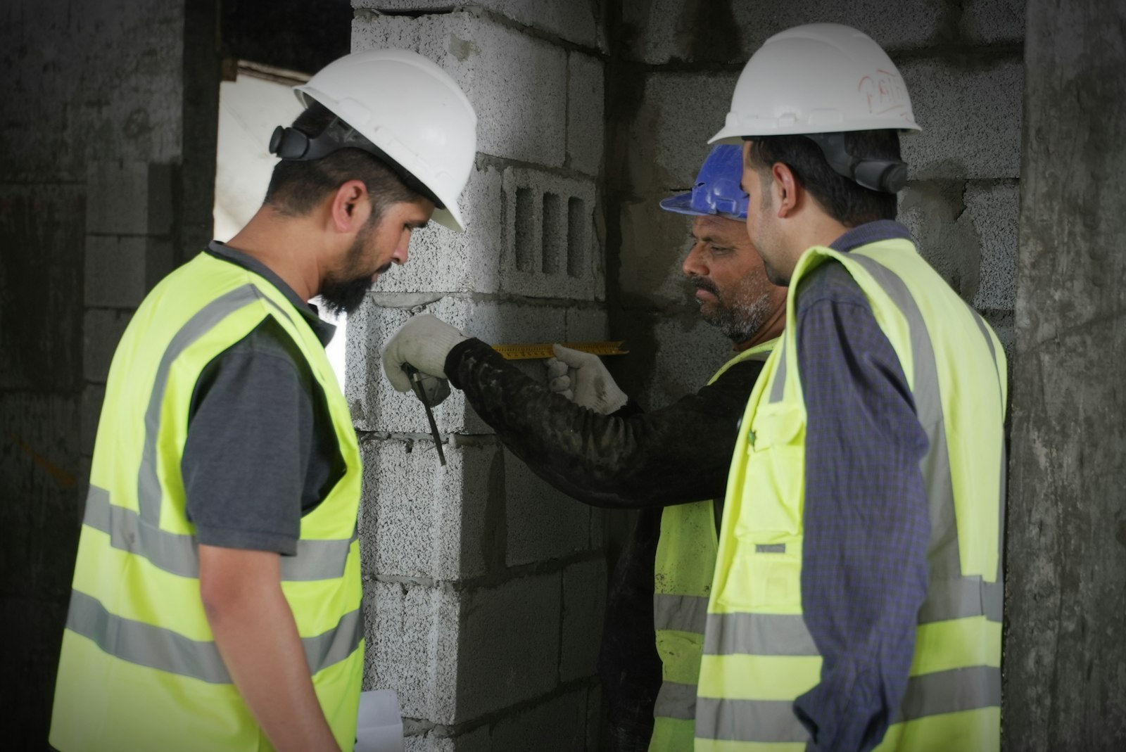 Inspectors in hard hats and safety vests measuring a block wall during a construction inspection